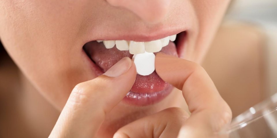 gros plan de mains féminines mettre une pilule ronde blanche sur la langue