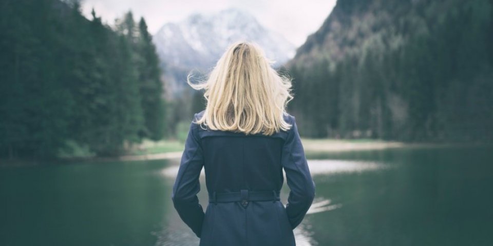 blonde woman standing backwards and watching magic lake in mountainous country landscape
