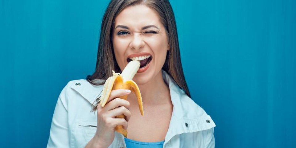 jeune femme, manger, banane, afin de se sentir heureuse fille tenant, fruit jaune, sur, dos bleu