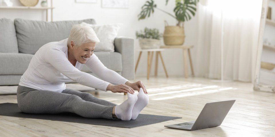 home sport active senior woman doing warming stretching exercises in front of laptop, training with online tutorials
