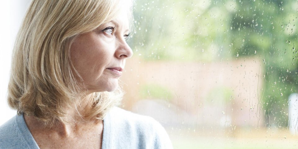 sad mature woman suffering from agoraphobia looking out of window