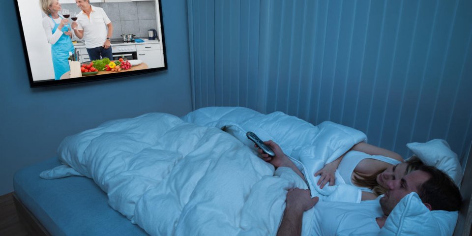 couple lying in bed with blanket watching television