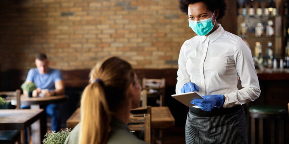 happy black waitress wearing protective face mask while taking order from customer on a touchpad in a cafe
