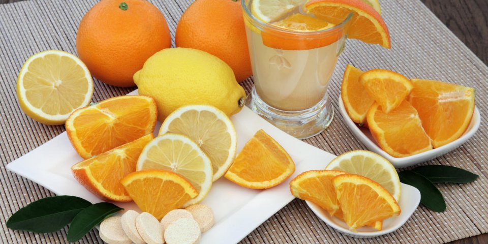cold and flu health remedy drink with orange and lemon fruit and vitamin c tablets on bamboo over oak background