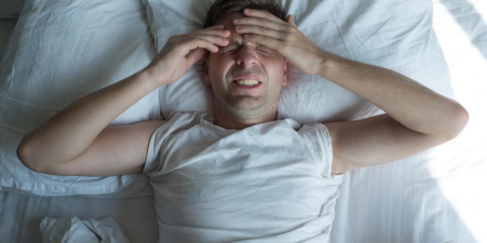 caucasian man lying in bed at home suffering from headache or hangover concept of problem with health