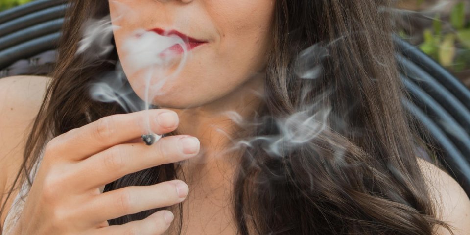belle jeune femme brune fumant une cigarette de marijuana médicale, avec la fumée coulant de sa bouche