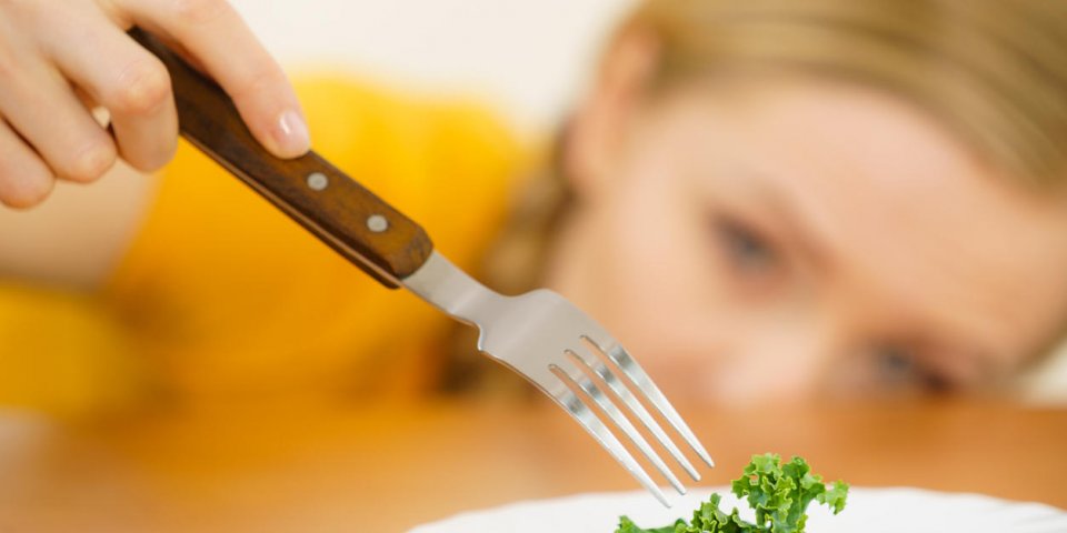sad young blonde woman dealing with anorexia nervosa or builimia having small green vegetable on plate dieting problems, ...