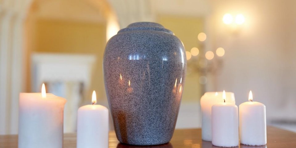 funeral, cremation and mourning concept - funerary urn and candles on table burning in church