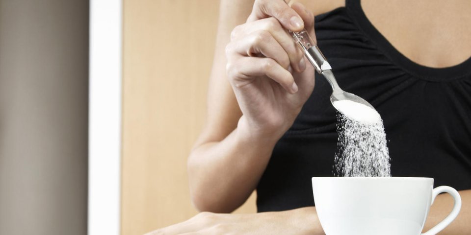 closeup of a cropped woman pouring sugar into tea cup