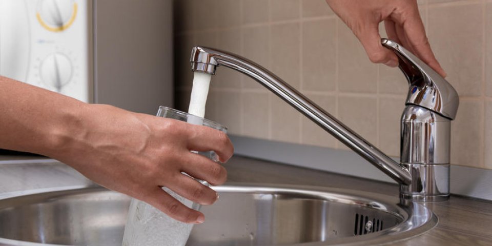 une femme, verser l'eau du robinet mélangeur dans un verre dans une cuisine
