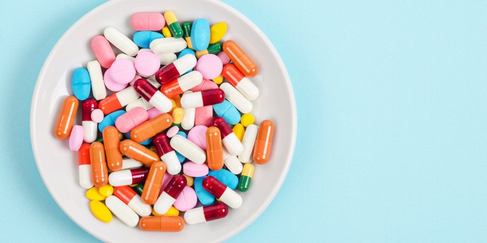 a top view of colourful medicine pills and capsules in white plate on blue background copy space for the ads