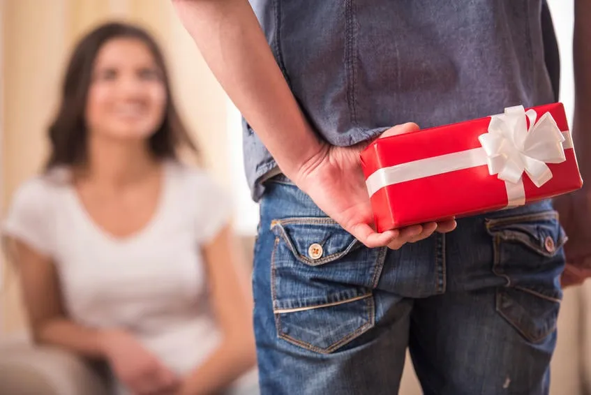 guy tient le cadeau derrière lui essaye de surprendre son attend petite amie à la maison se concentre sur le garçon