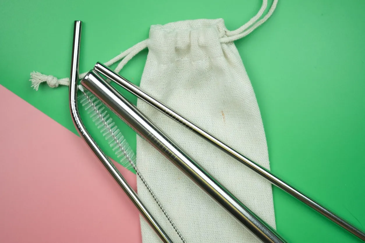 reusable stainless steel straws and cleaning brush in white cotton bag on pink and green background concept of eco friendly lifestyle