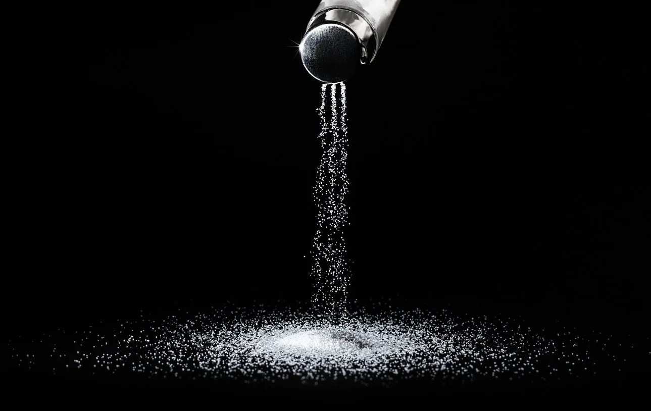 salt spills out of the salt shaker in thin streams on a black backgroundconcept salting