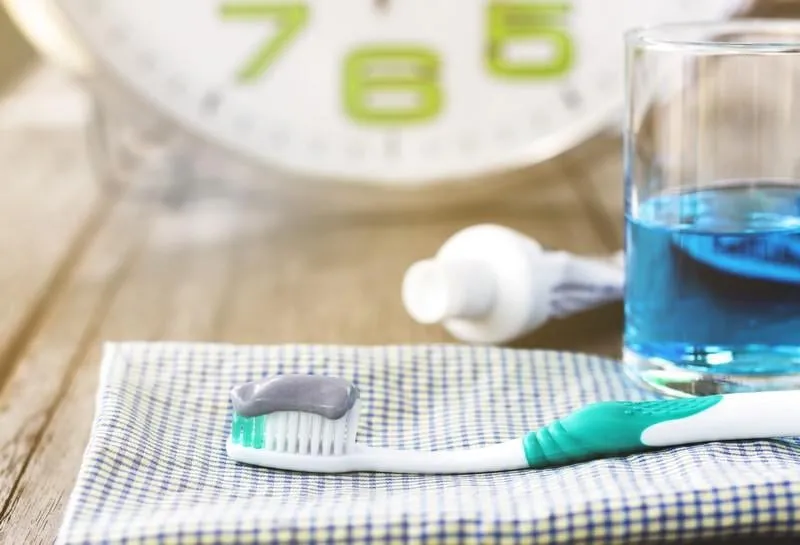 herbal toothpaste with a new toothbrush and a blue mouthwash on wall clock background dental care concept