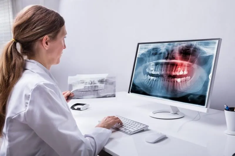 mature female dentist looking at teeth x-ray on computer in clinic