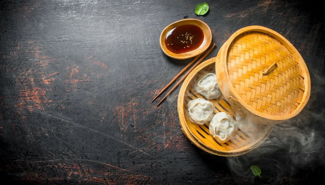 hot aromatic manta dumplings in bamboo steamer with soy sauce on dark rustic background