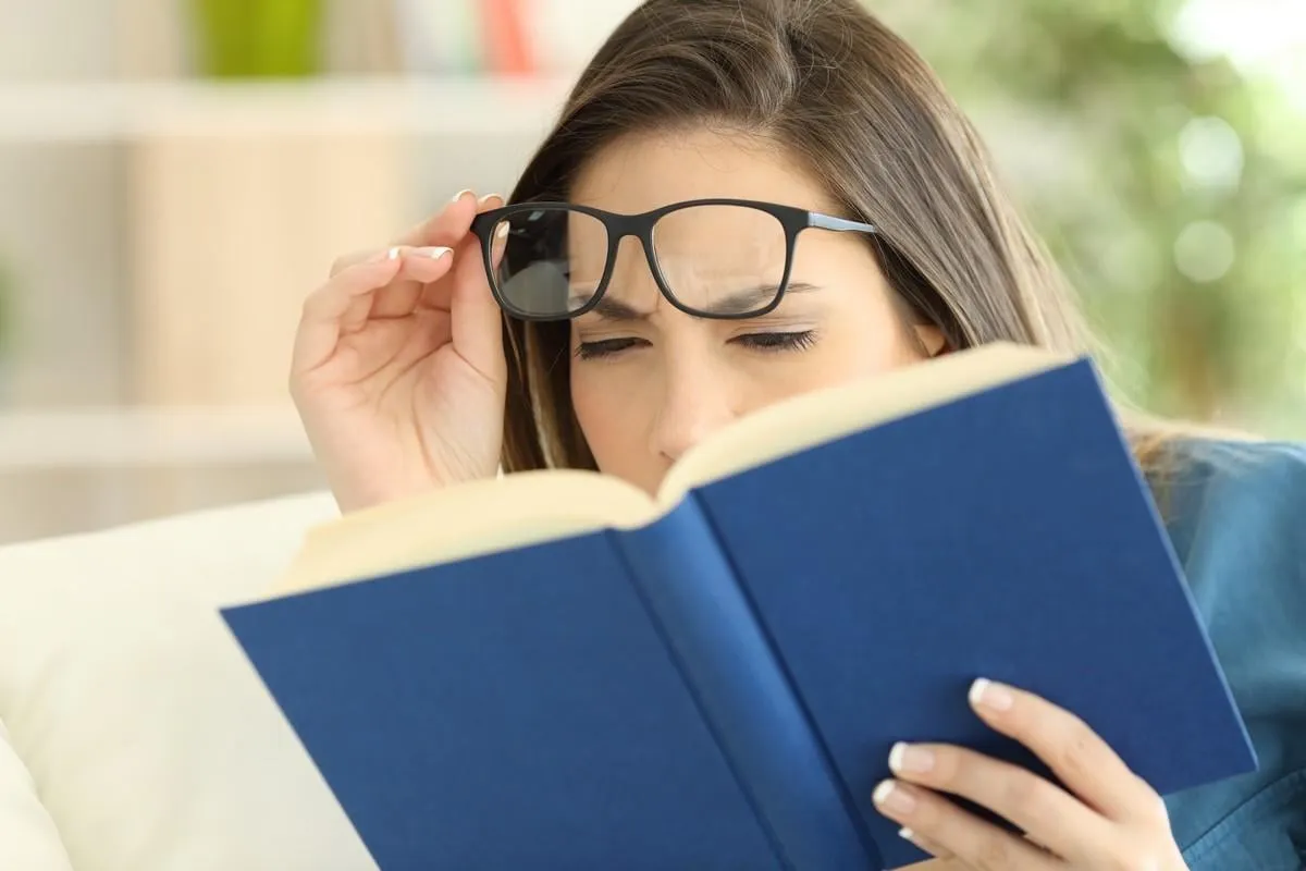 woman suffering eyestrain trying to read a book at home