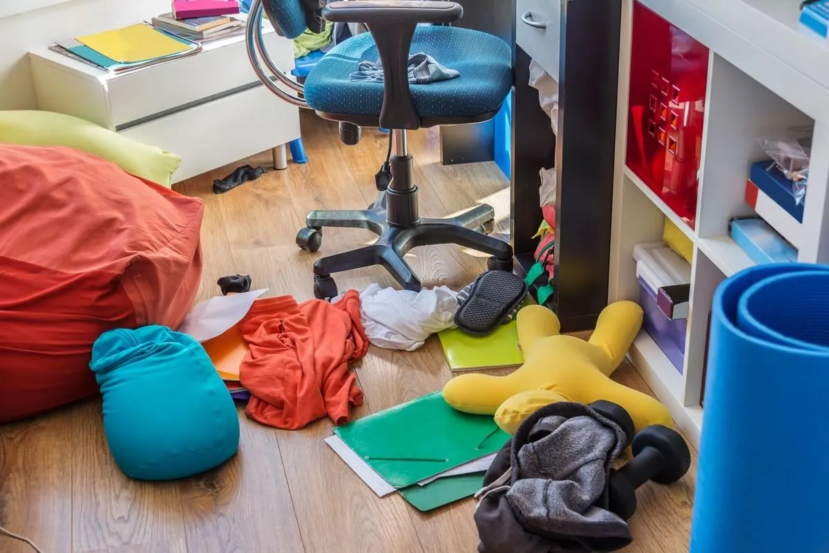 boy messy bedroom with clothes and colorful pillows on the floor