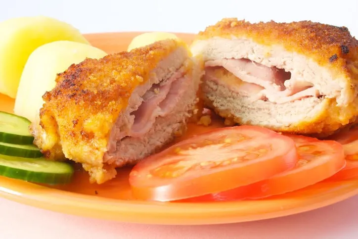 cordon bleu servi sur une assiette orange avec pommes de terre et légumes frais et coupé au milieu