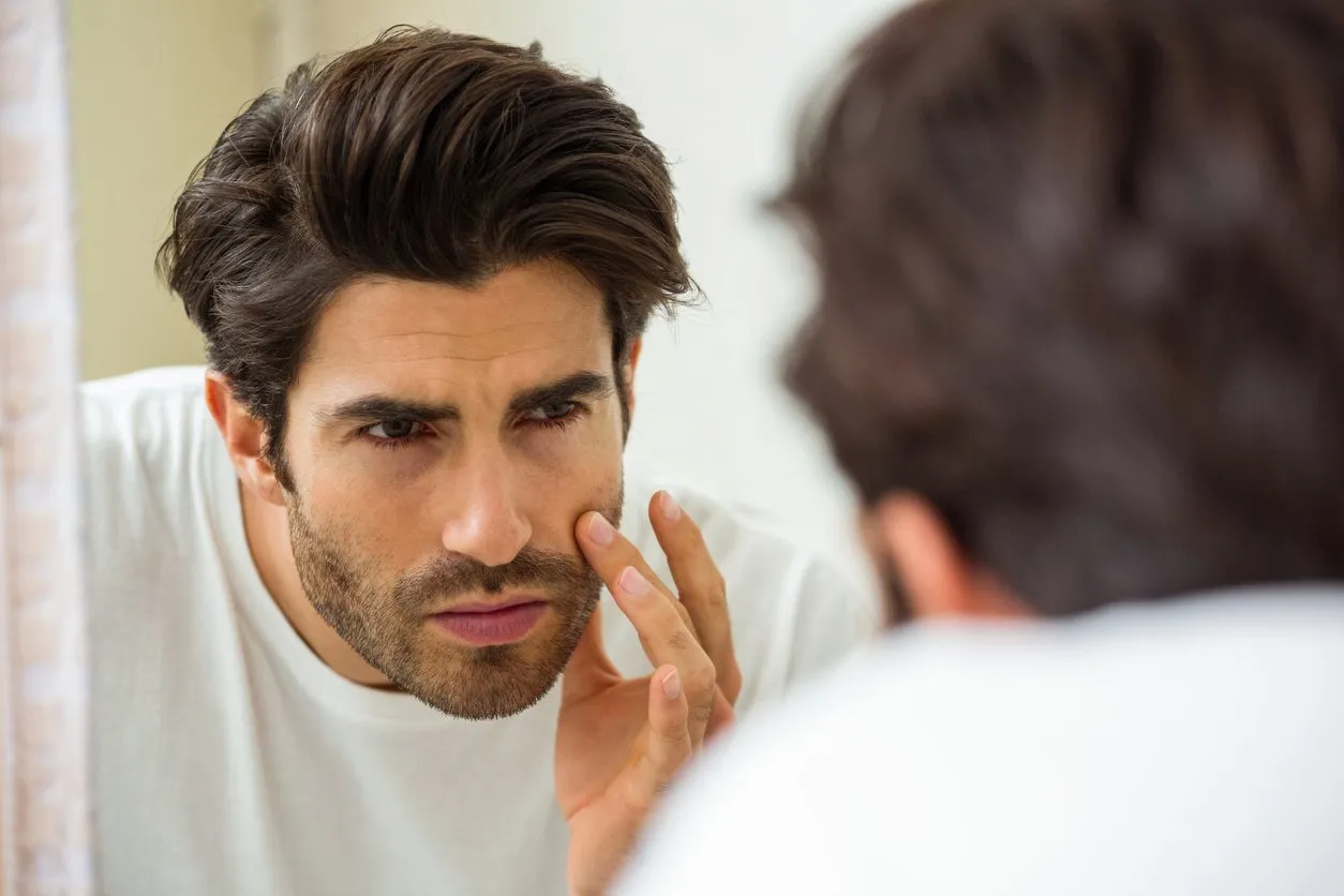 man looking in mirror and checking his skin in bathroom
