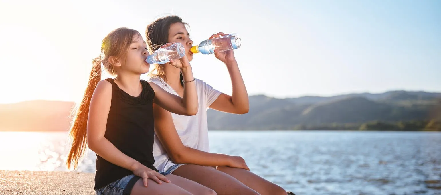 deux filles, boire de l'eau et assis au bord de la mer