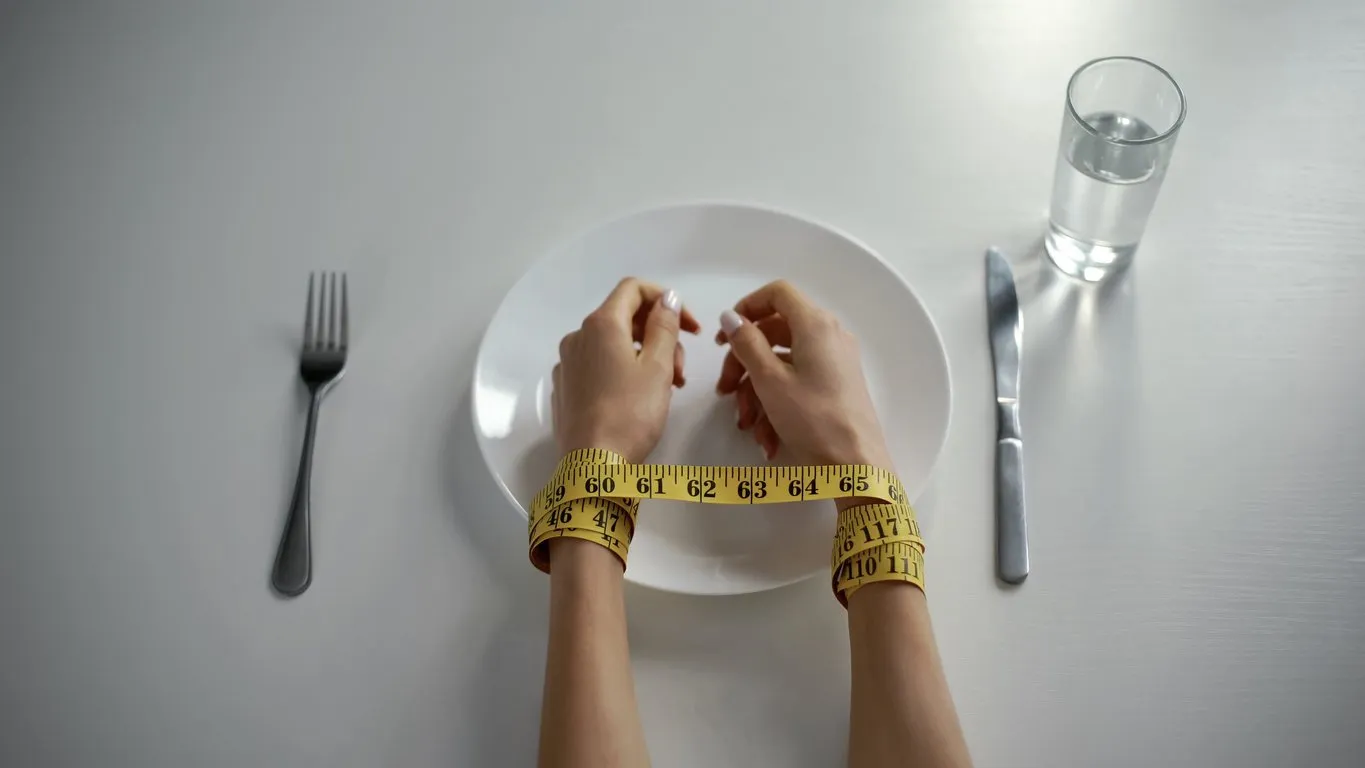 hands tied with tapeline on empty plate, girl obsessed with counting calories