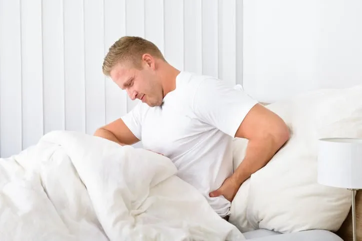 portrait de jeune homme assis sur un lit souffrant de maux de dos