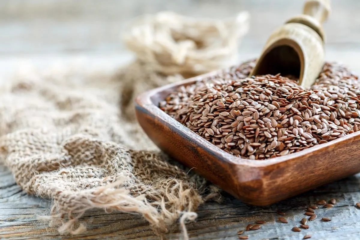 flax seeds and wooden scoop in bowl on old sacking close up, selective focus