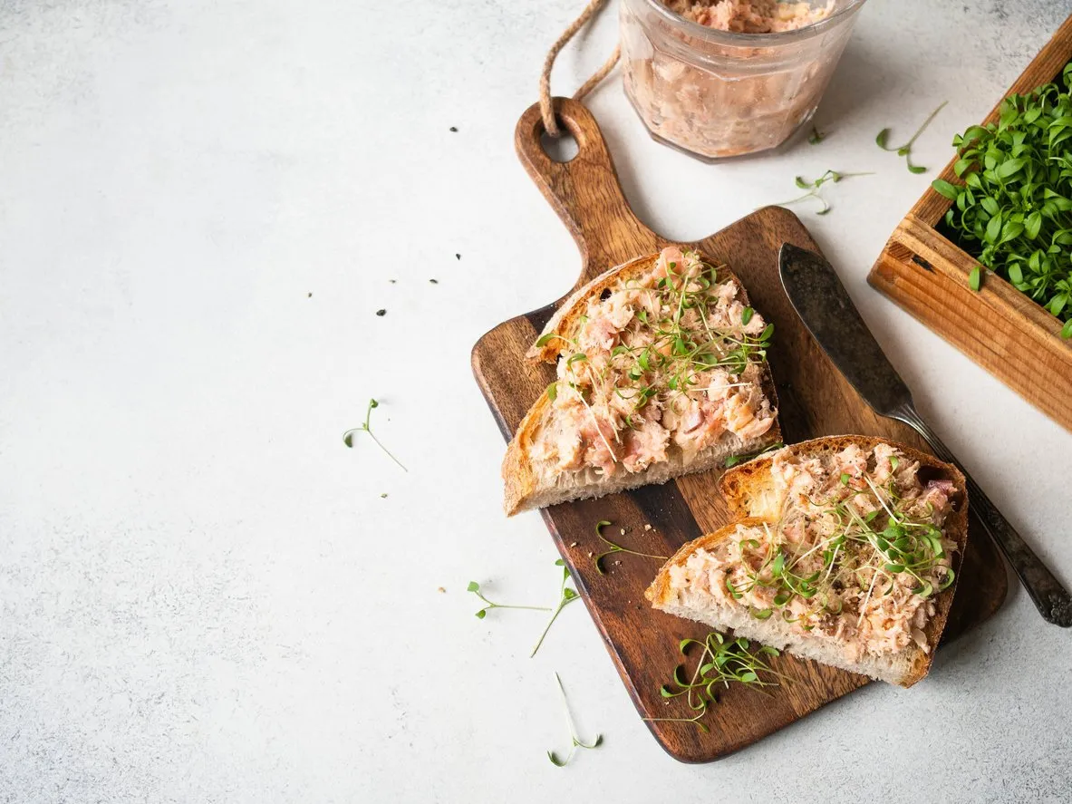 healthy toasts with salmon pate and fresh green sprouts on yeast-free bread on wood cutting board on grey background copy space