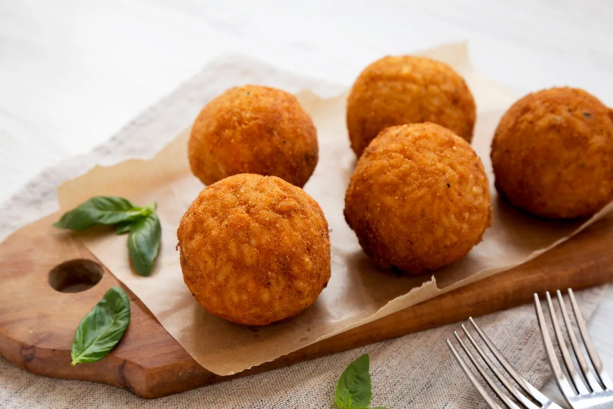 homemade fried arancini with basil on a rustic wooden board, side view italian rice balls close-up