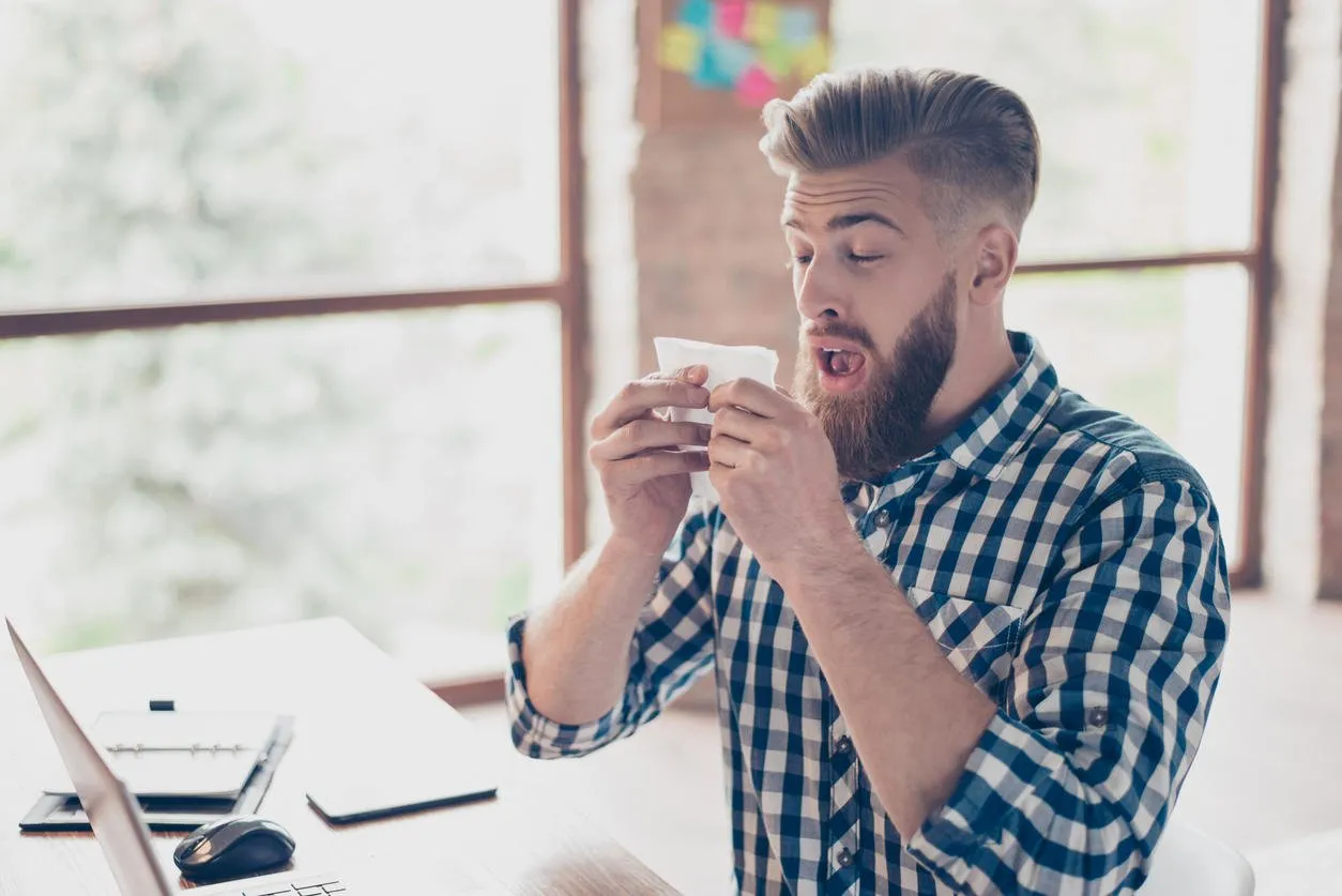 sad upset ill handsome attractive coughing with high temperature closed eyes manager business businessman freelancer feeling discomfort using paper tissue checkered casual shirt light modern office