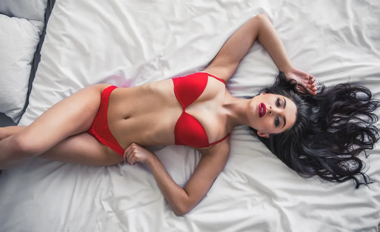 the young sexy girl in red lingerie, lying on a bed in a bedroom at home