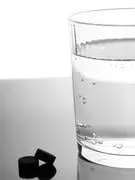 comprimés de charbon et verre d'eau sur fond glacé