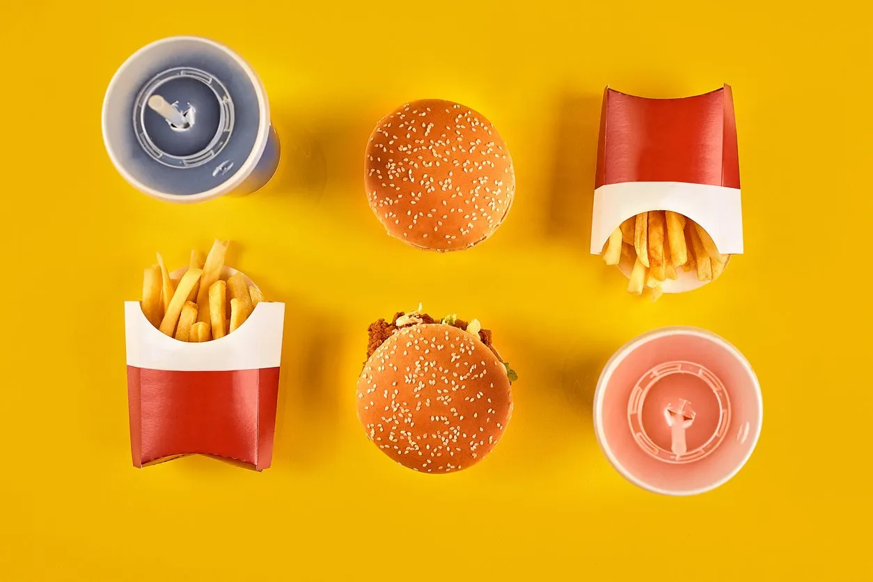 fast food and unhealthy eating concept - close up of fast food snacks and cold drink on yellow background top view copy space still life flat lay