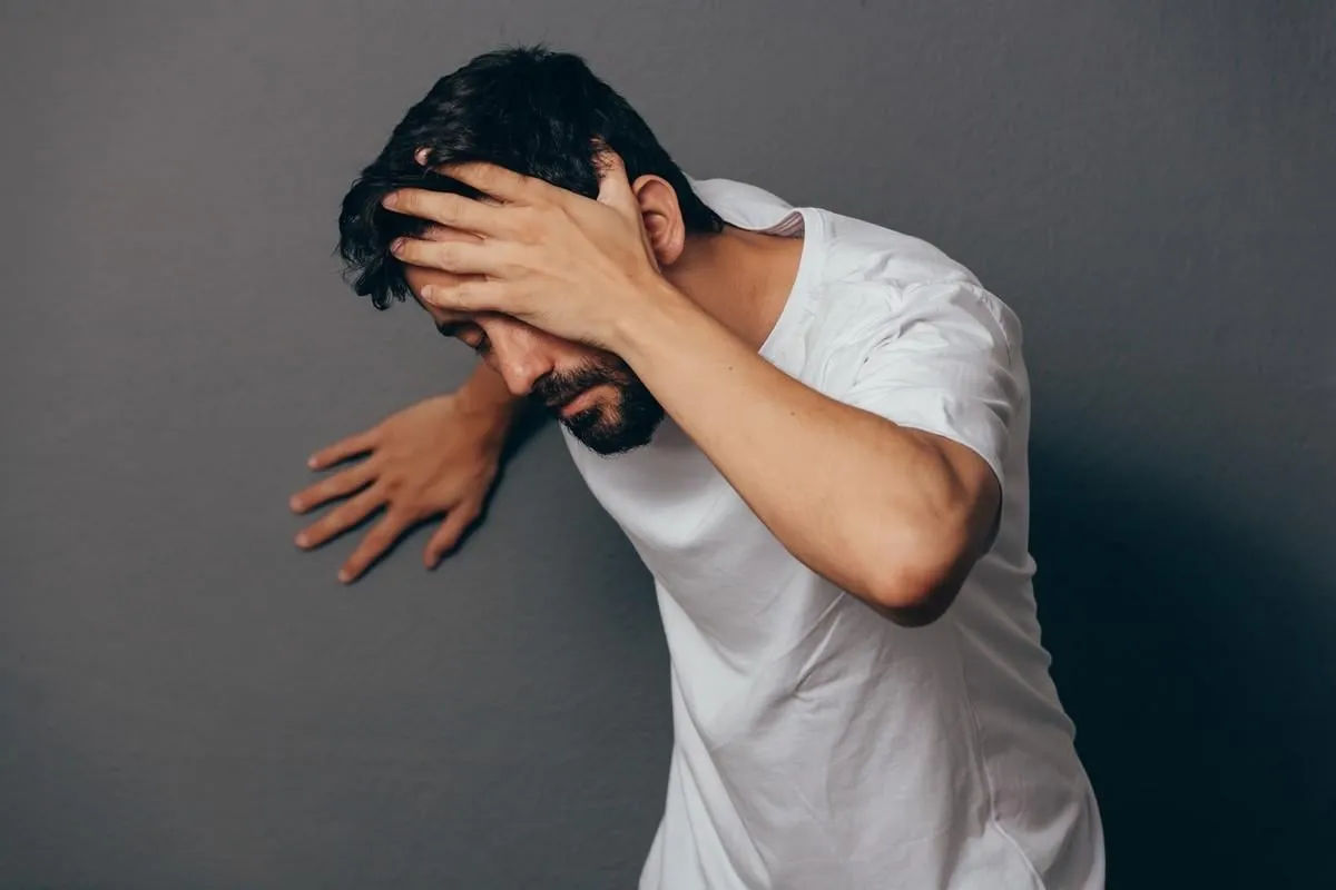 man suffering from dizziness with difficulty standing up while leaning on wall