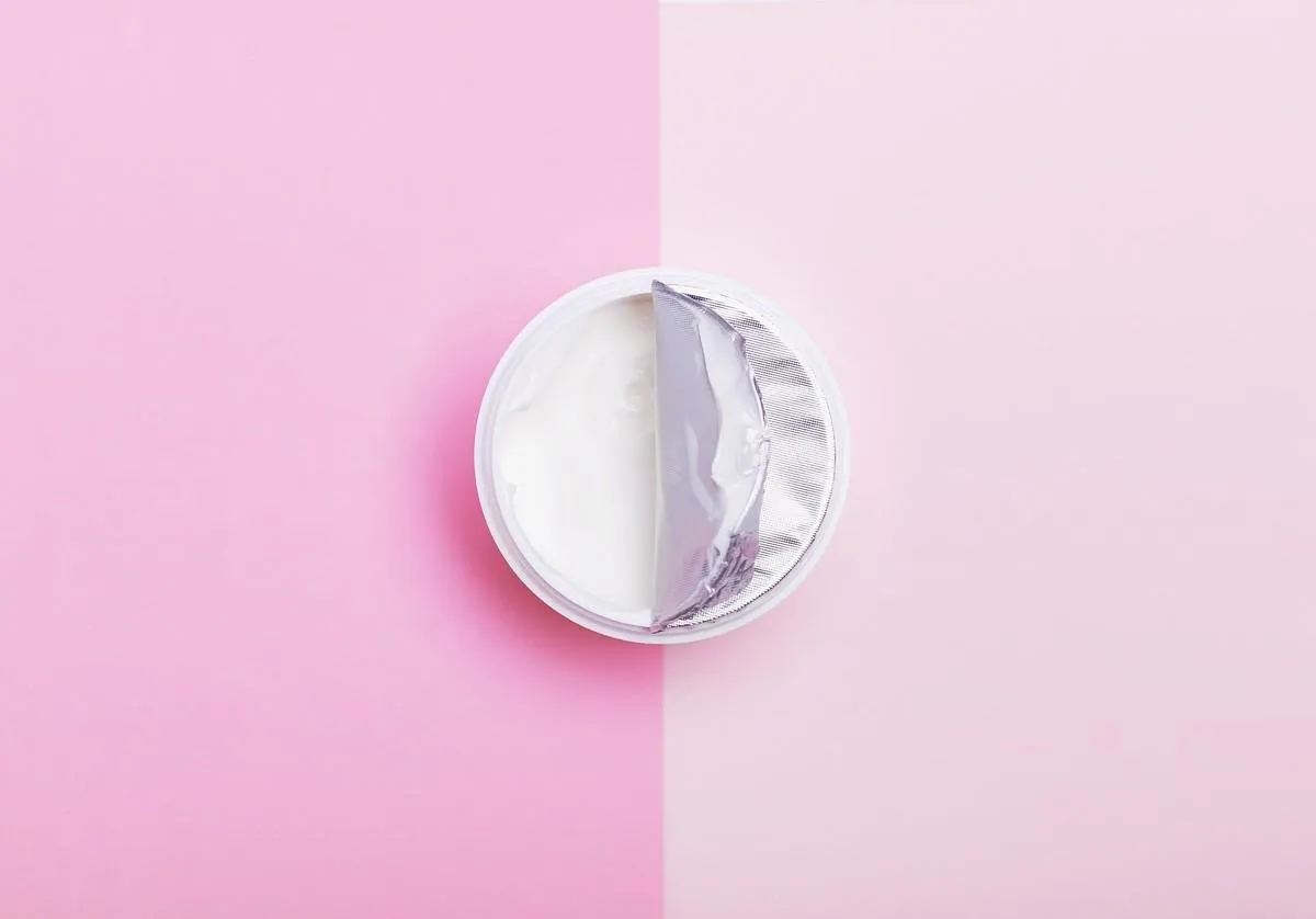 moisturizer with half open lid on light pink background flat lay top view