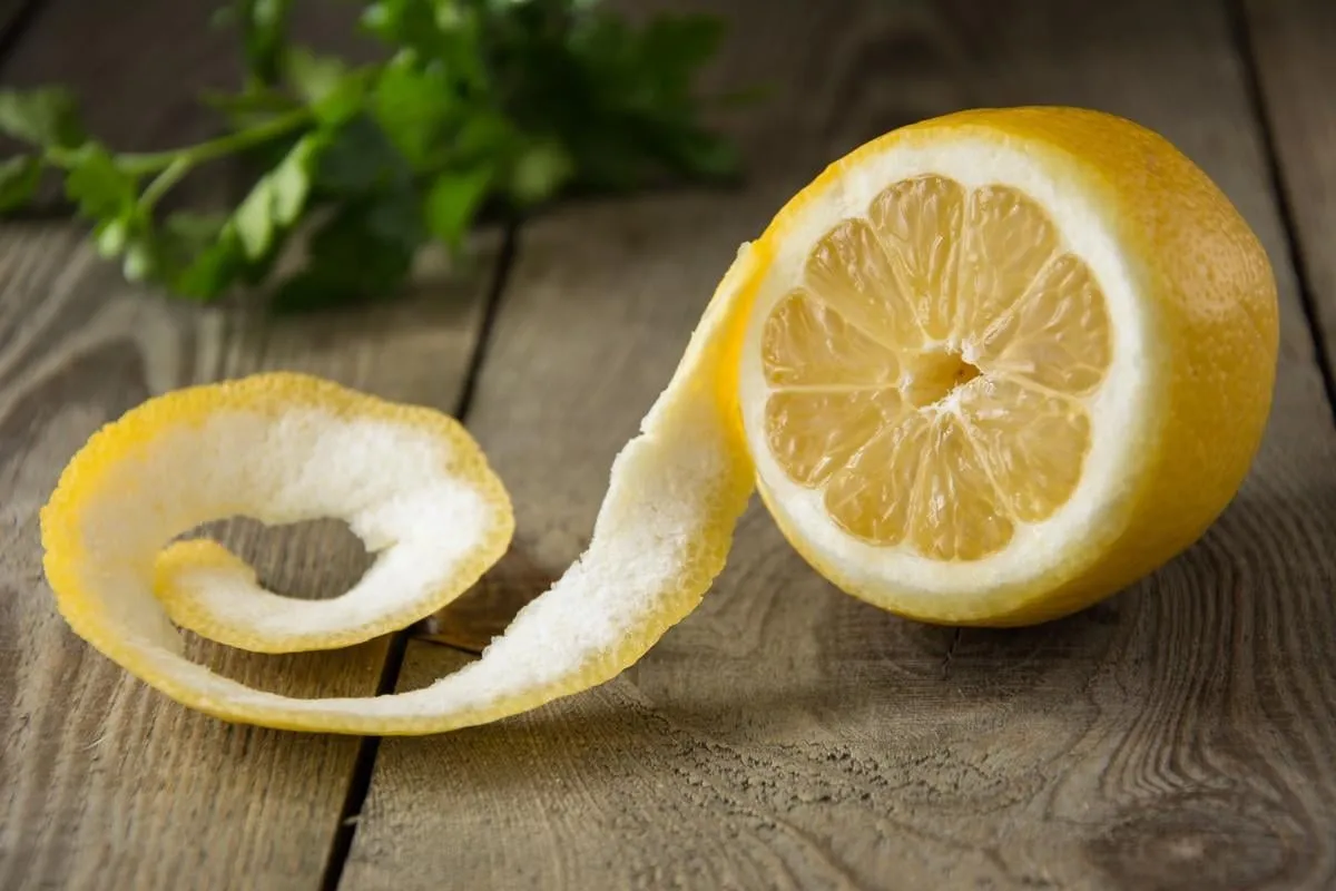 half peeled fresh lemon on a wooden table with green herbs in the background