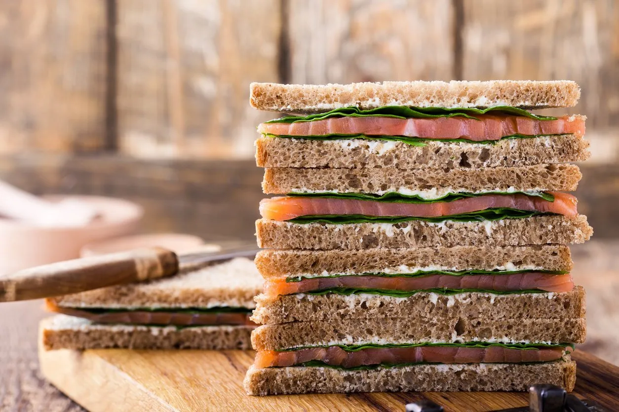 healthy vegetarian sandwiches with smoked salmon and greens toasts on cutting board over rustic wooden background, close up, selective focus