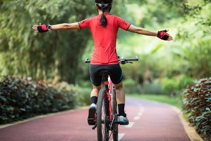 woman cyclist riding mountain bike on tropical rainforest trail with arms outstretched