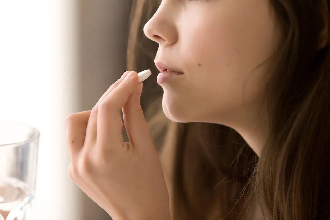 close up image of woman putting white round pill in mouth sick female taking medicines, antidepressant, painkiller or antibiotic young lady drinking contraceptives pharmacy and healthcare concept