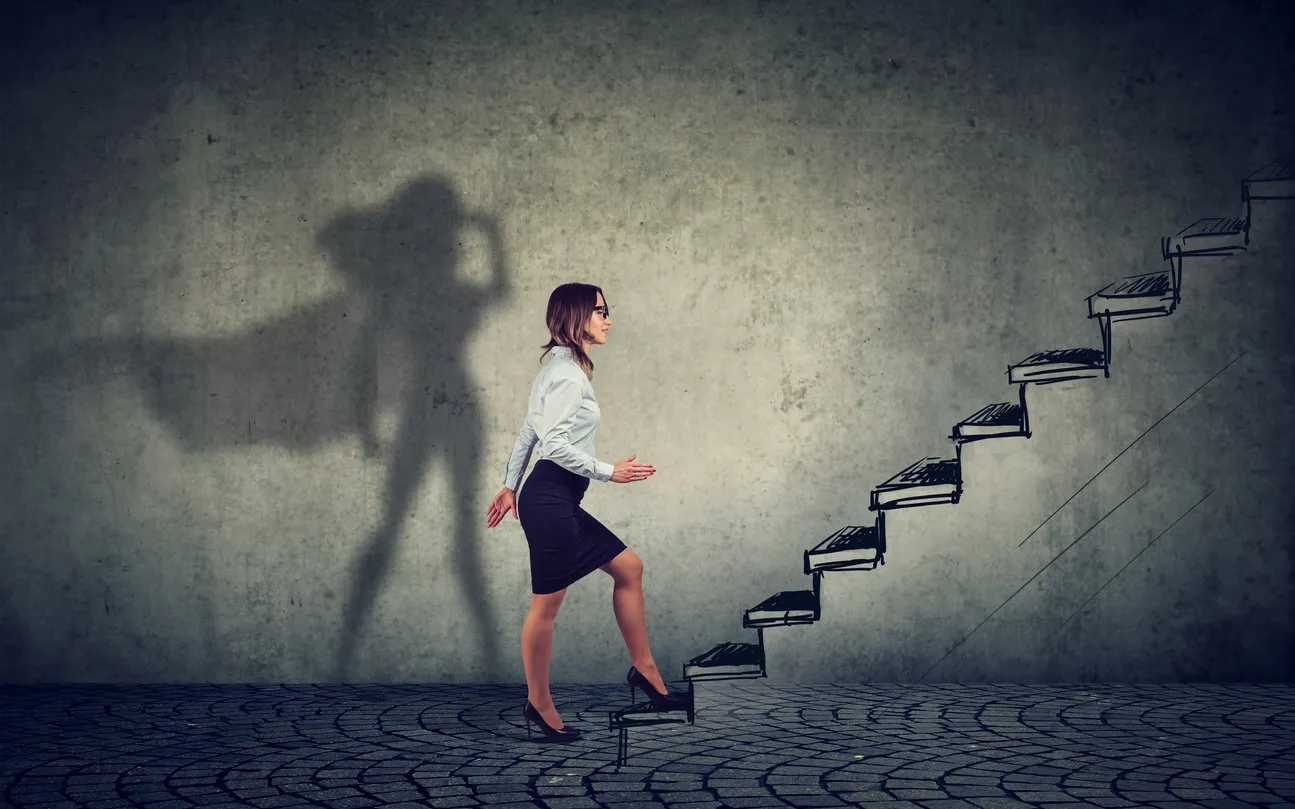 super hero business woman stepping up on stairs climbing to success on gray wall background