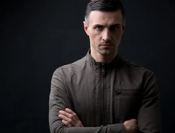 confiant, jeune homme, à, bras, plié, debout, sur, arrière-plan noir, regarder appareil-photo