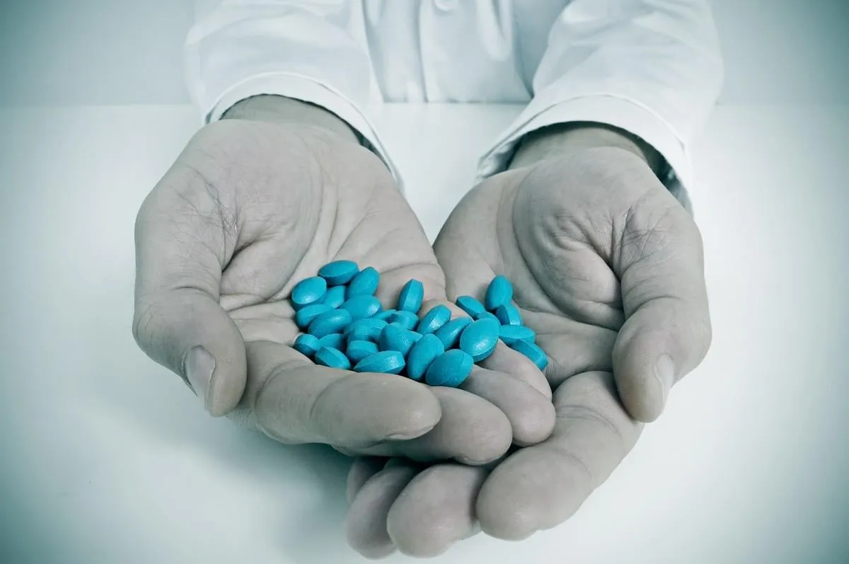 a doctor sitting in a desk with a pile of blue pills in his hands