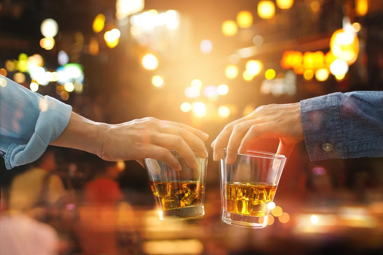 cheers clinking of friends with bourbon whisky drink in party night after work on colorful background
