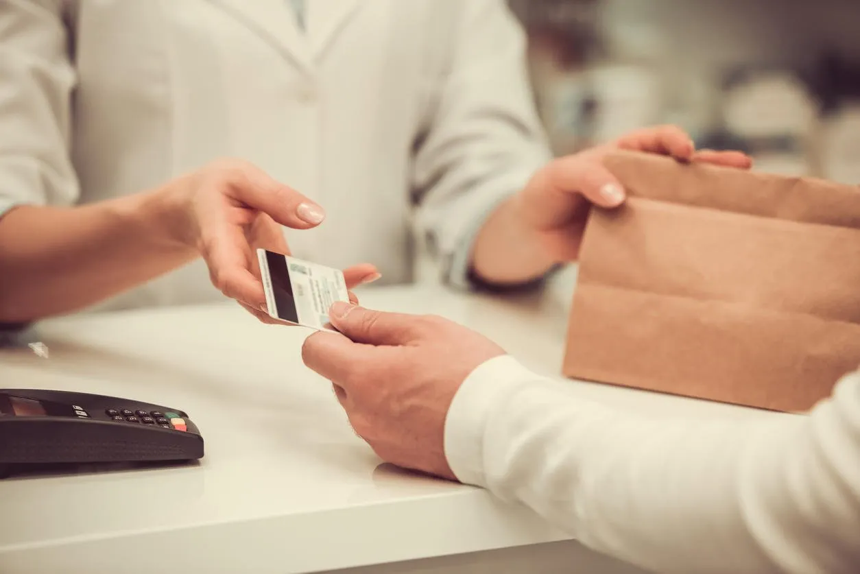 cropped image of pharmacist giving a purchase to a client and talking a credit card while working at the cash desk in pharmacy