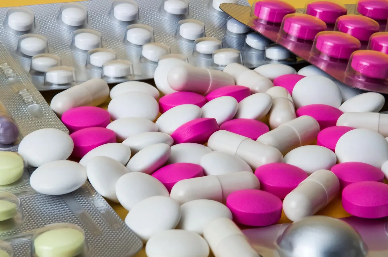 white and pink tablets are scattered among blisters with other pills large