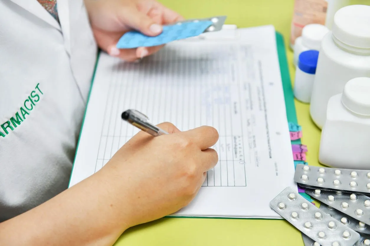 close-up view of female doctor hand holding pills pack and writing prescription healthcare, medical and pharmacy concept