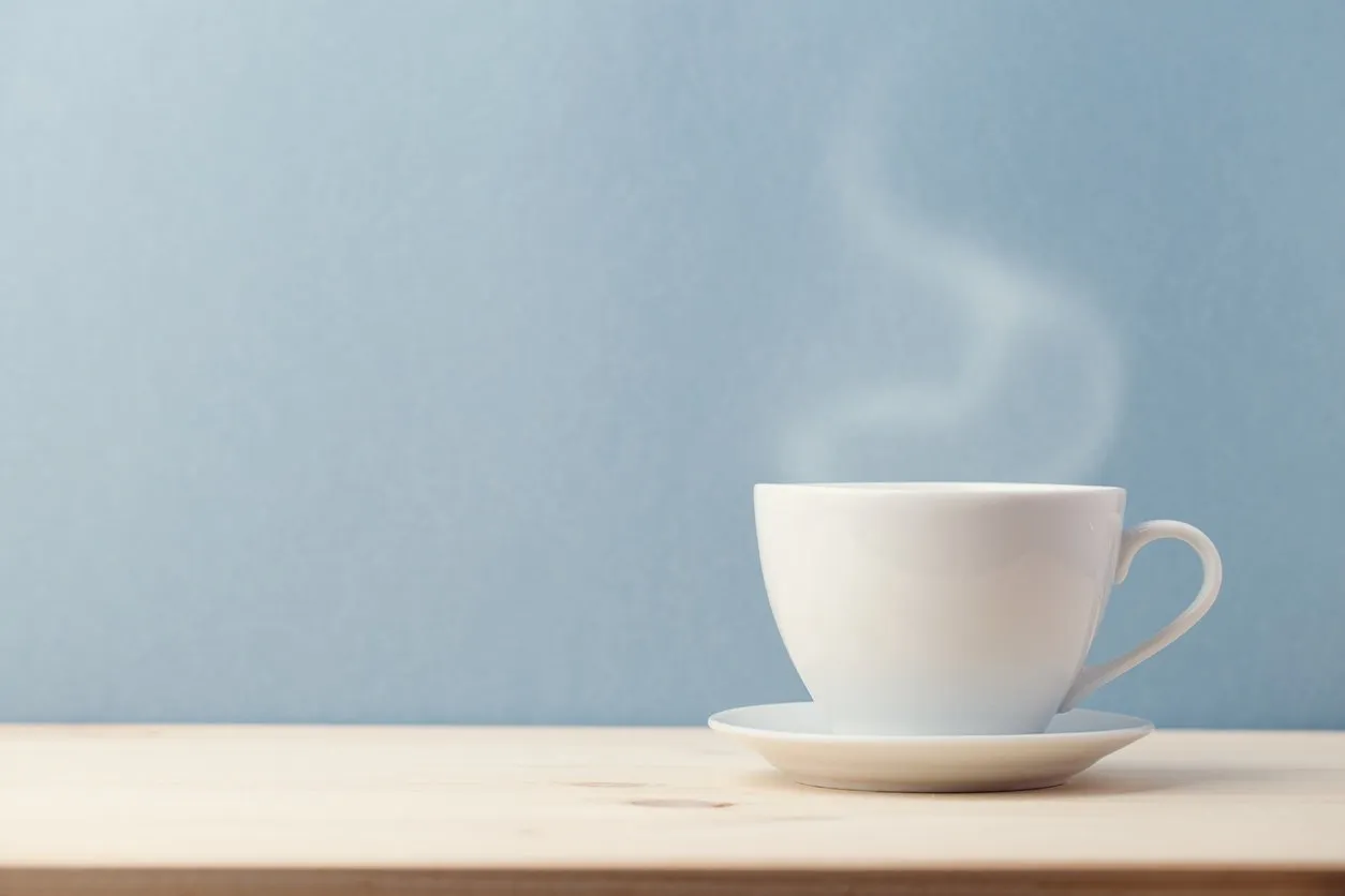 small white cup on saucer with steam coming from hot delicious drink on blue background