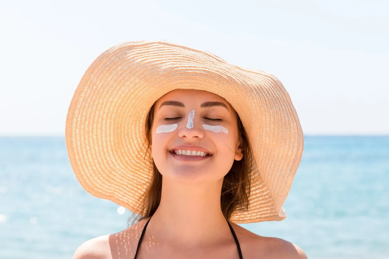 beautiful young woman in hat is applying sunblock under her eyes and on her nose like indian sun protection concept
